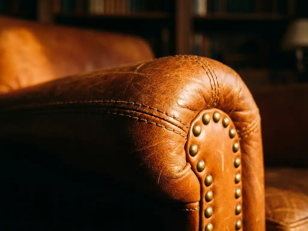 Luxury cognac leather armchair showing hand-stitched seams, brass studs, and rich grain texture in detailed close-up view.