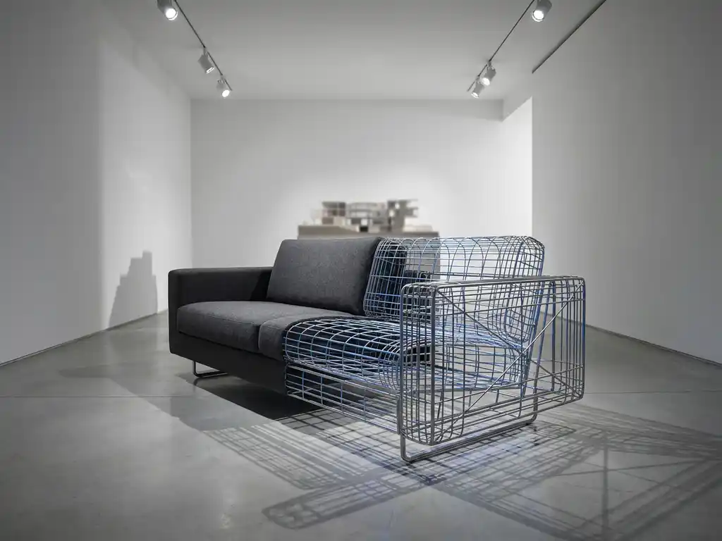 Modern sofa with exposed wireframe structure showing 3D mesh geometry beneath fabric upholstery in minimalist showroom